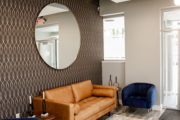 The Soothing Dental lounge, with a leather sofa, a round gold mirror and a blue armchair by the window