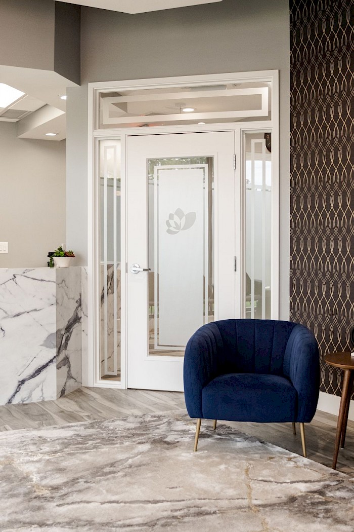 A blue velvet armchair beside the frosted glass door at the entrance to the Soothing Dental lounge