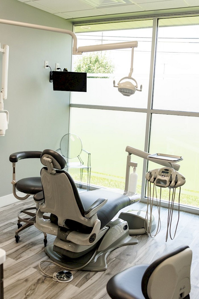 A sage green treatment room at Soothing Dental, with the chair and overhead light by the window