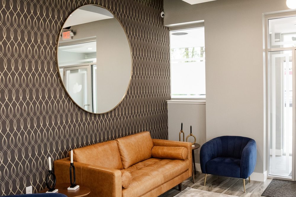 The Soothing Dental lounge, with a tan leather sofa and a round gold mirror on patterned wallpaper